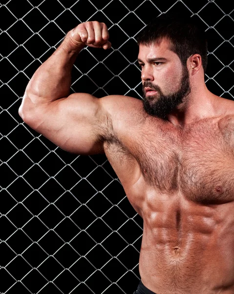 Bodybuilder posing in front of chain link. — Stock Photo, Image