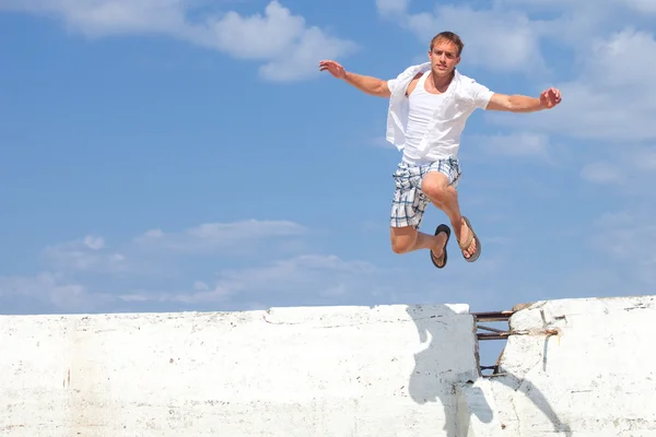 stock image A young man leaping over a wall outside.