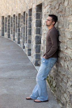 genç adam ayakta outsitde duvarın önünde.
