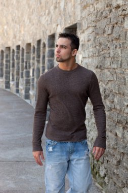 outsitde taş duvar önünde yürüyen genç adam.