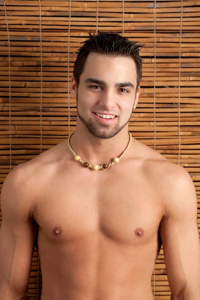 Attractive man, shirtless, in front of bamboo screen. — Stock Photo, Image