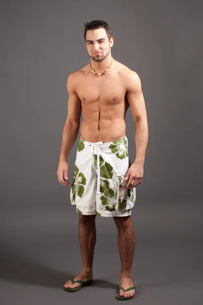 Attractive young man in boardshorts. Studio shot over grey. — Stock Photo, Image