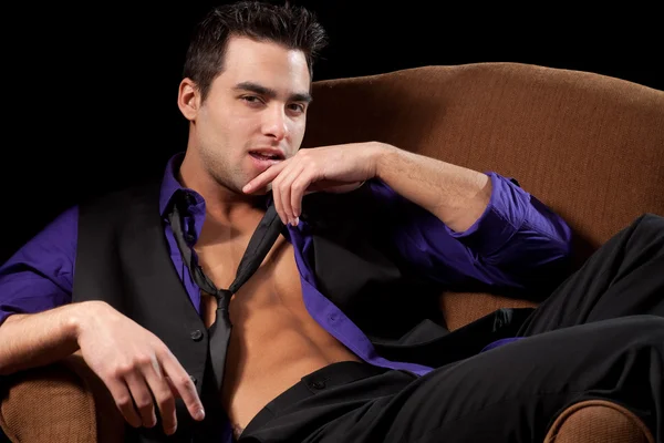 Well dressed man in chair, shirt open. Studio shot over black. — Stock Photo, Image