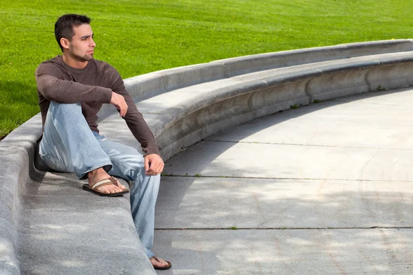 stock image Young man sitting outsitde on concrete bench.