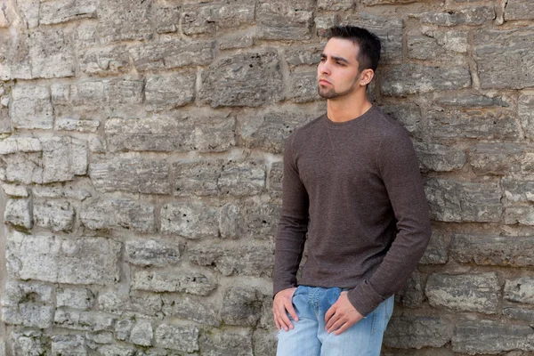 Νεαρός άνδρας outsitde στέκεται μπροστά από το πέτρινο τοίχο. — Φωτογραφία Αρχείου