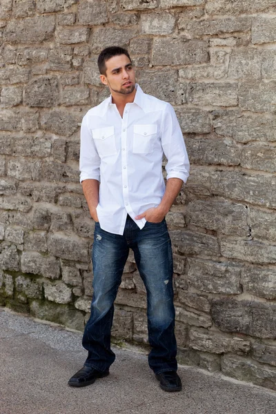 Молодой человек стоит снаружи перед каменной стеной . — стоковое фото