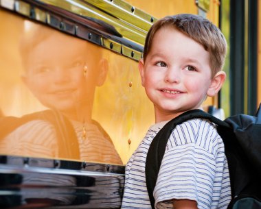 Young boy with nervous smile waits to board bus on first day of school. clipart