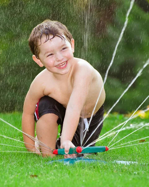 Jovem menino fora jogando no aspersor de água — Fotografia de Stock