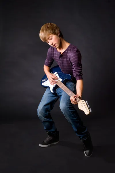 stock image Young man playing on guitar on dark background