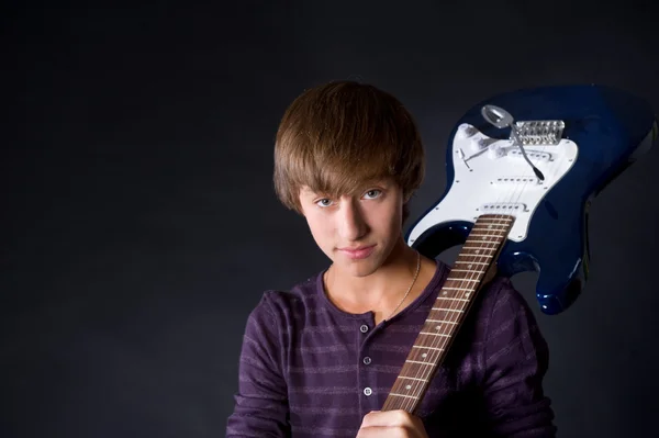 Mladý muž s kytarou na tmavém pozadí — Stock fotografie