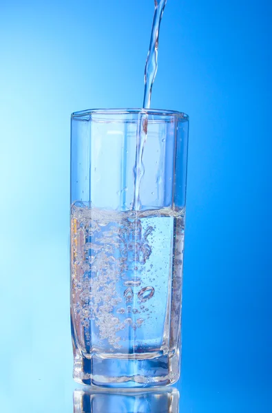 Despejando água em vidro sobre fundo azul — Fotografia de Stock