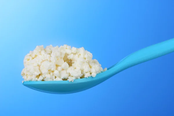 Tasty cottage cheese in spoon on blue background — Stock Photo, Image