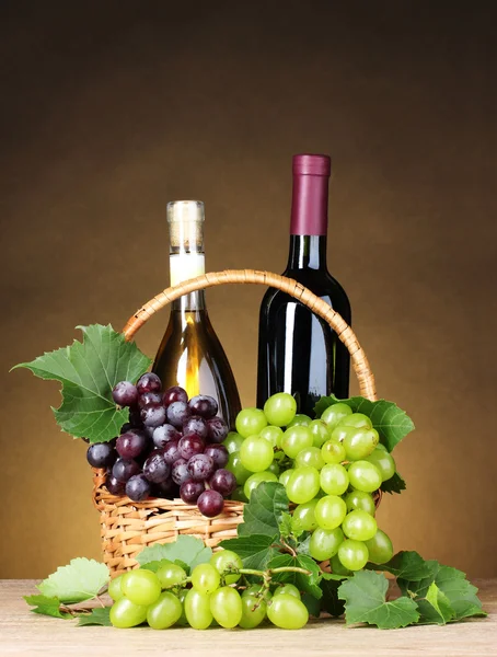 Бутылки вина и винограда в корзине на желтом фоне — стоковое фото
