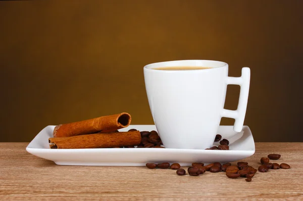 Tasse Kaffee, Kaffeebohnen und Zimt auf Holztisch auf braunem Hintergrund — Stockfoto