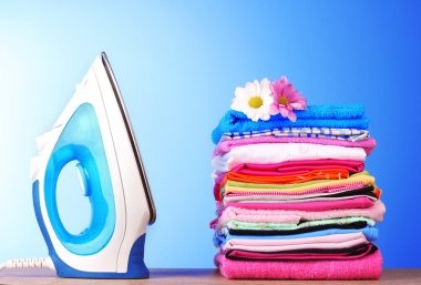 Pile of colorful clothes and electric iron on blue background