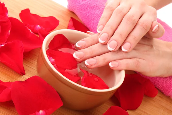 Hände mit französischer Maniküre entspannen in einer Schüssel Wasser mit Rosenblättern — Stockfoto