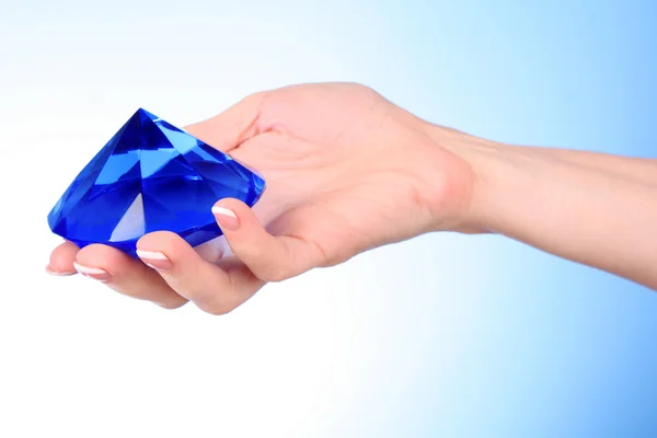 Žena ruku s velkým modrý krystal na modrém pozadí — Stock fotografie
