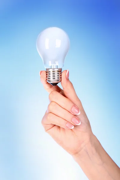 Mão com lâmpada no fundo azul — Fotografia de Stock