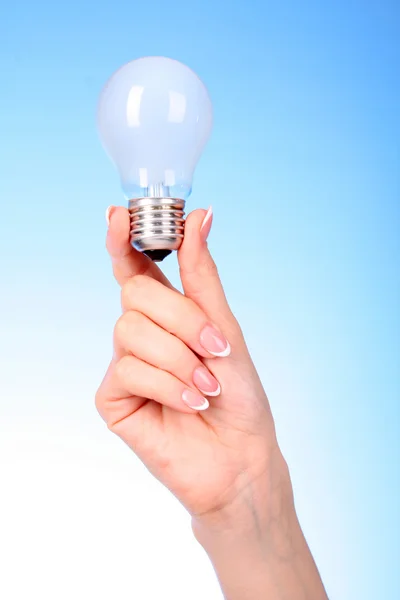 Donna mano con lampada a incandescenza su sfondo blu — Foto Stock