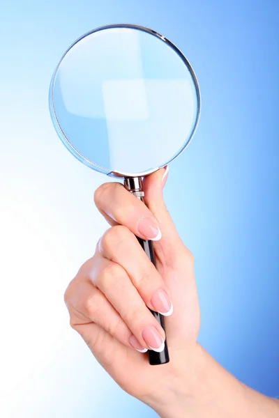 青色の背景に拡大鏡を女性の手 — ストック写真