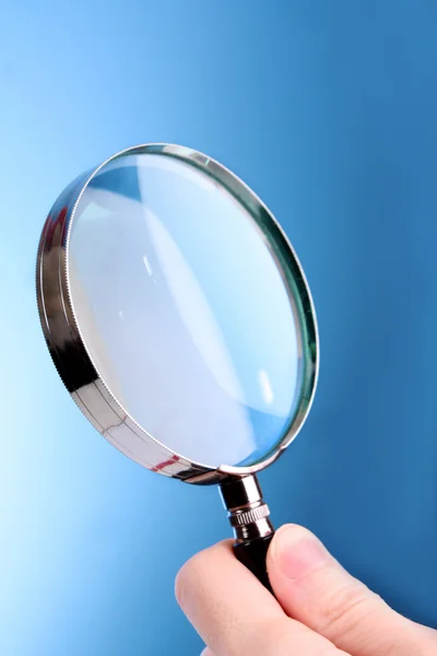 Magnifying glass in woman hand on blue background — Stock Photo, Image