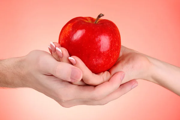 Apple mellan man och kvinna hand på röd bakgrund — Stockfoto