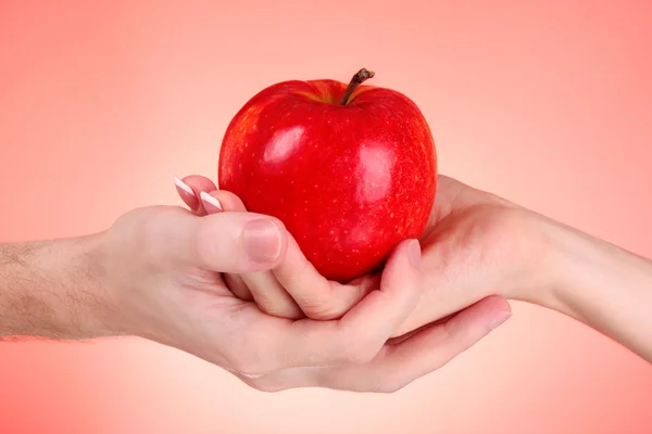 Manzana entre hombre y mujer mano sobre fondo rojo — Foto de Stock