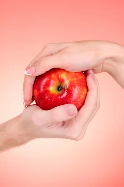 Jabłko między mężczyzną i kobietą ręką na czerwonym tle — Zdjęcie stockowe