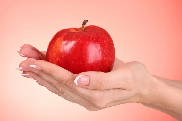 Mãos de mulher segurando uma maçã no fundo vermelho — Fotografia de Stock