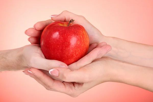 Mulher e homem mãos segurando uma maçã no fundo vermelho — Fotografia de Stock