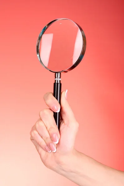 Magnifying glass in woman hand on red background — Stock Photo, Image