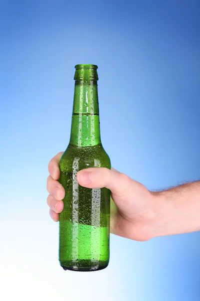 Flasche Bier in der Hand auf blauem Hintergrund — Stockfoto