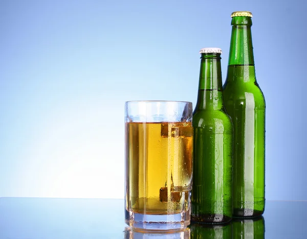 Bottiglie con birra e tazza su sfondo blu — Foto Stock
