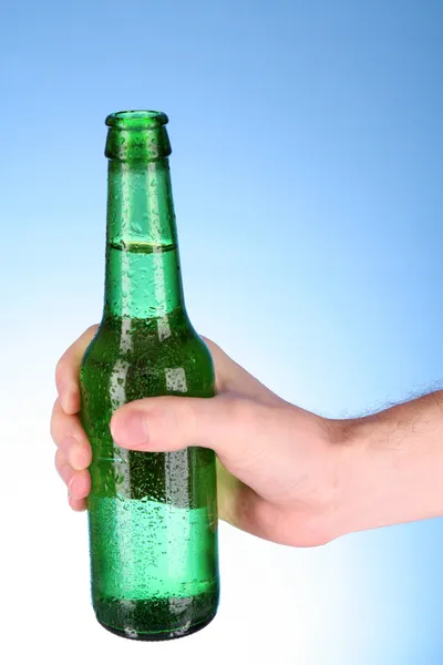 Garrafa de cerveja na mão sobre fundo azul — Fotografia de Stock