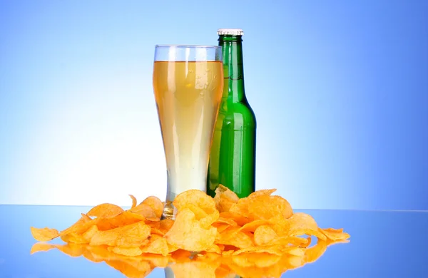 Botella con cerveza, taza y papas fritas sobre fondo azul — Foto de Stock
