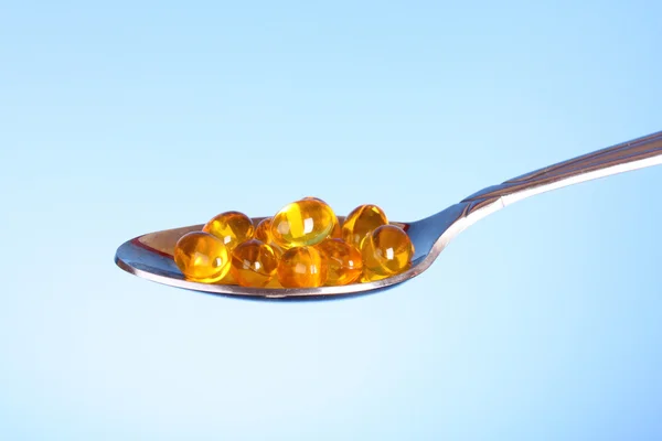 A spoon full of Fish Oil Capsules on blue — Stock Photo, Image