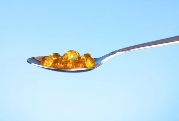 A spoon full of Fish Oil Capsules on blue — Stock Photo, Image