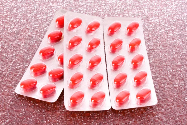 Cápsulas vermelhas de vitaminas em um fundo marrom — Fotografia de Stock