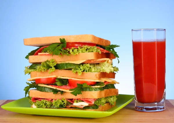 Huge sandwich and glass of tomato juice on blue background — Stock Photo, Image