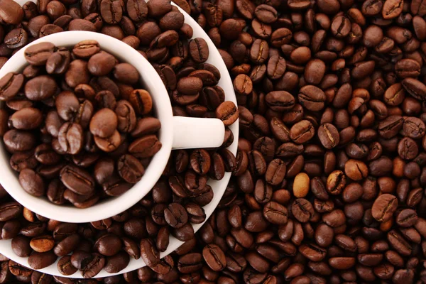 Liten vit kopp kaffe med kaffe korn på spannmål bakgrund — Stockfoto