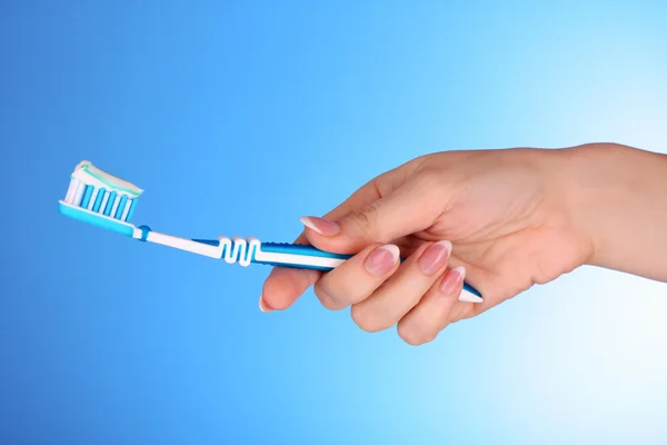Borstel voor tandpasta op in het meisje de hand op blauwe achtergrond — Stockfoto