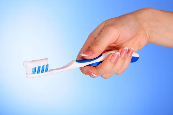 Borstel voor tandpasta op in het meisje de hand op blauwe achtergrond — Stockfoto