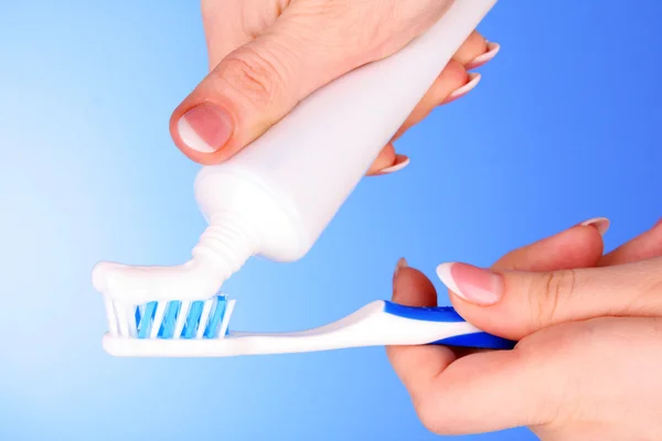 Pasta de dente e escova na mão sobre fundo azul — Fotografia de Stock