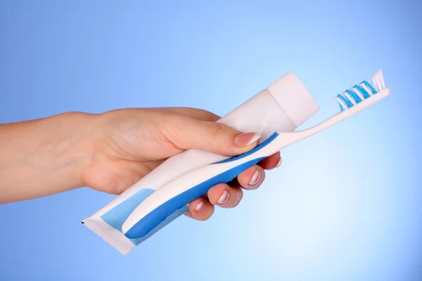 Pasta de dente e escova na mão sobre fundo azul — Fotografia de Stock
