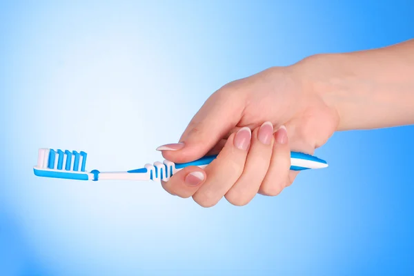 แปรงยาสีฟันในมือของผู้หญิงบนพื้นหลังสีฟ้า — ภาพถ่ายสต็อก