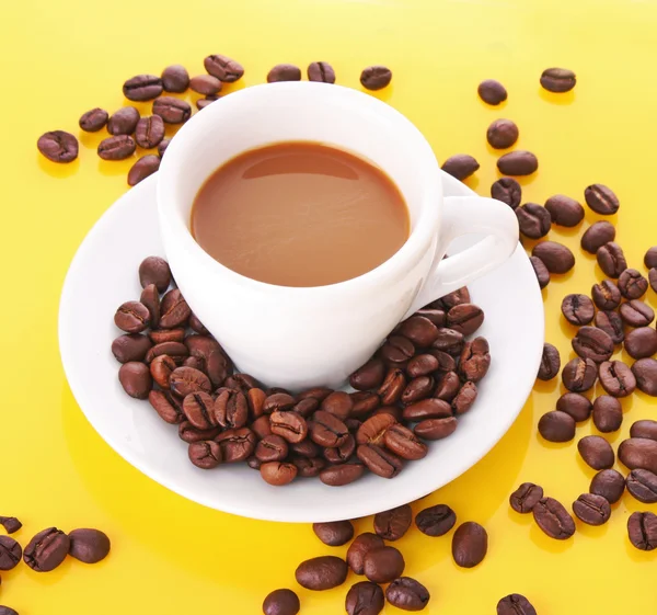 Kleine weiße Tasse Kaffee mit Kaffeekorn auf gelbem Hintergrund — Stockfoto