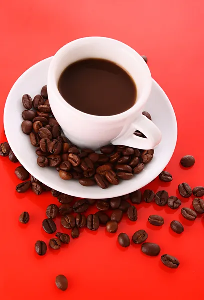 Kleine weiße Tasse Kaffee mit Kaffeekorn auf rotem Hintergrund — Stockfoto