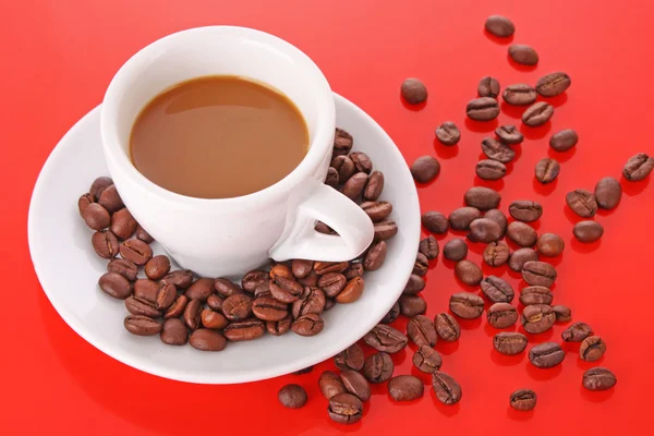 Petite tasse blanche de café avec grain de café sur fond rouge — Photo