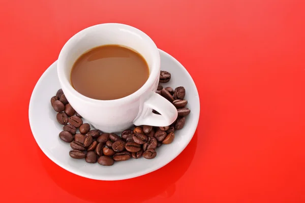 Petite tasse blanche de café avec grain de café sur fond rouge — Photo