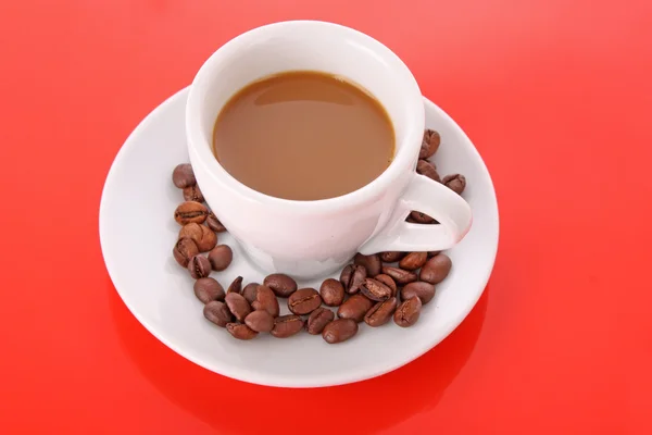 Small white cup of coffee with coffee grain on red background — Stock Photo, Image
